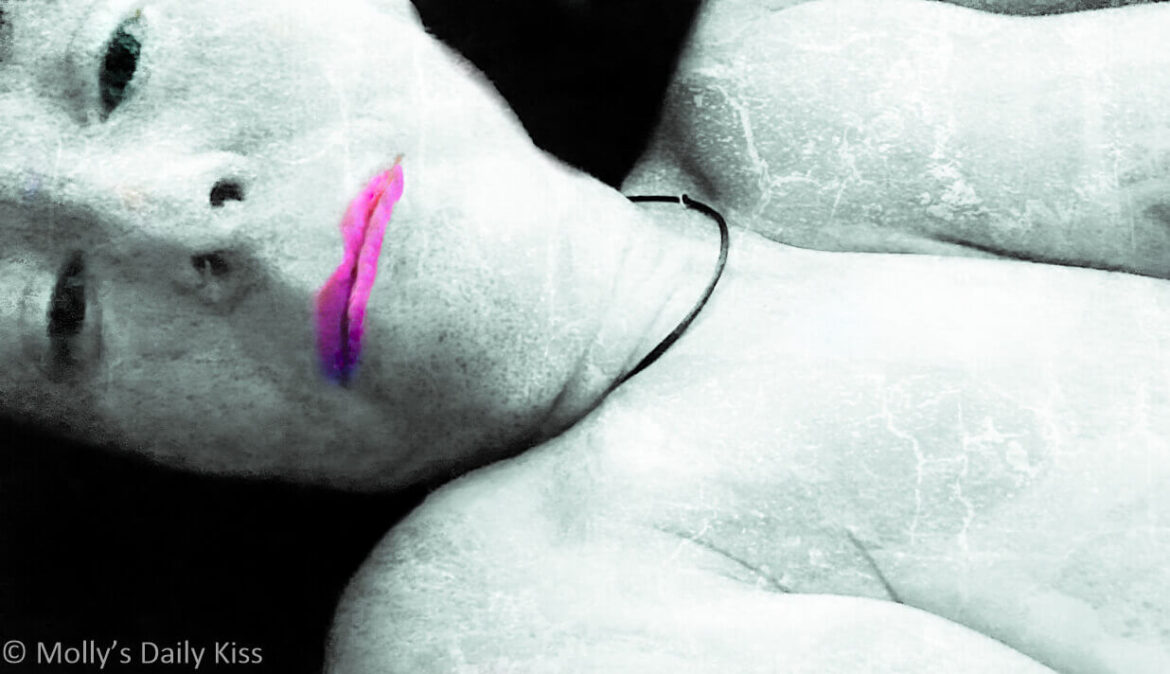 Molly laying looking up at the camera with cracked doll skin and black lifeless eyes and bright pink lips