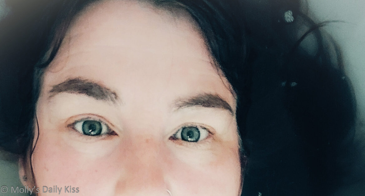 cropped image from the post of Looking down on Molly's face and breasts as she lays in the water. Her hair is swirling round her head in the water and her green eyes are looking up into the camera for post called mermaid