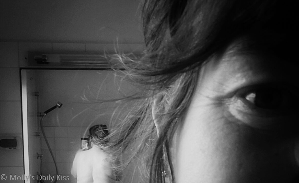 Cropped Black and white image looking over Molly's shoulder to her bare back and bum reflected in mirror on the other side of the room. In the right of the image we can see half of molly's face and she is smiling
